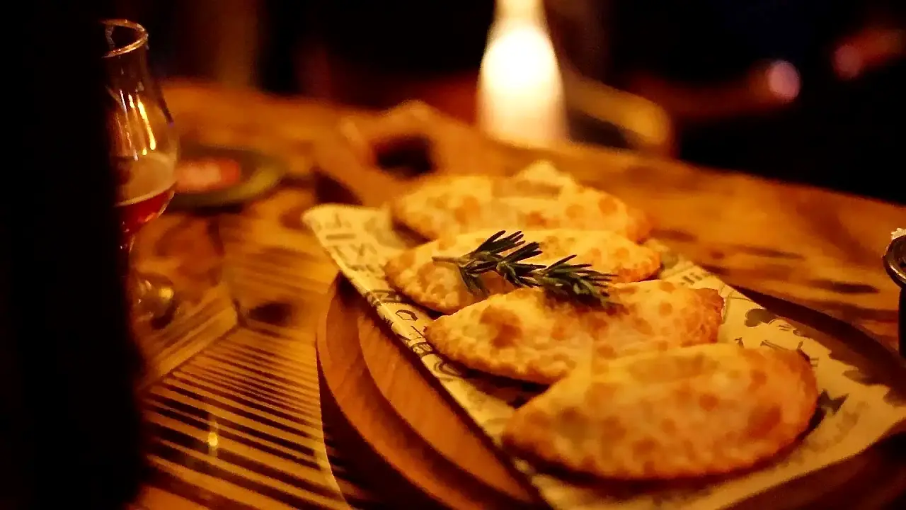 Golden baked Argentine empanadas with rosemary on a wooden board at Klandestino Lounge, North Miami
